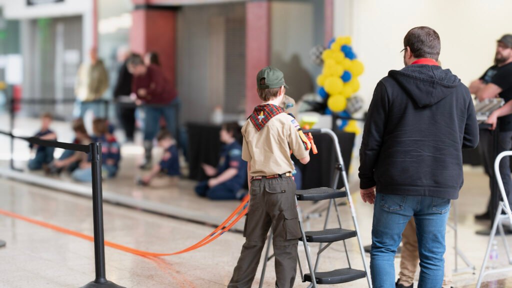 A cub scout places his Hot Wheels car on the track after racing his pinewood derby car.